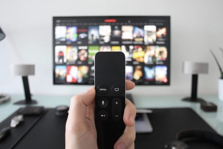 Hand holding a streaming remote in front of a TV