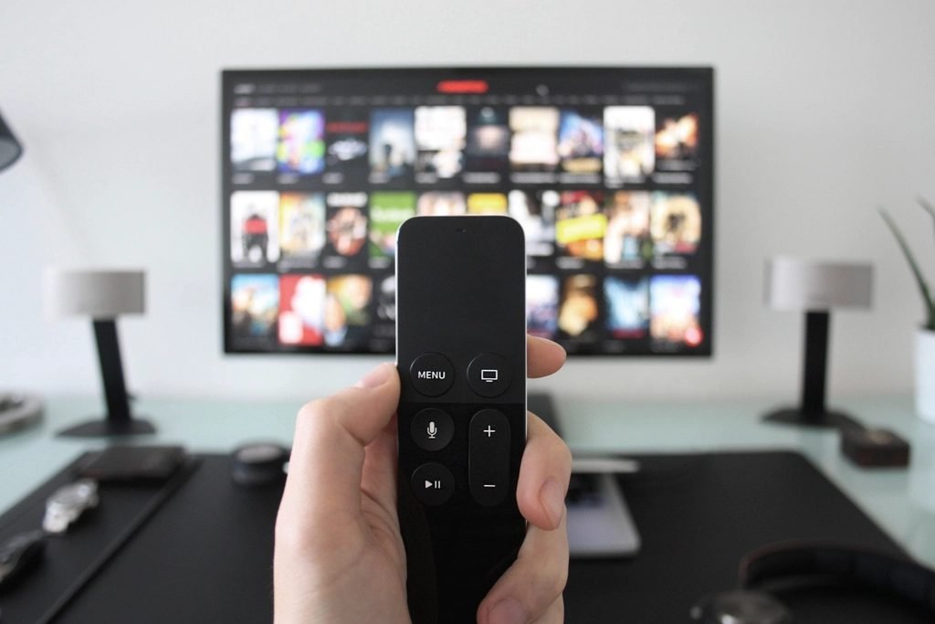 Hand holding a streaming remote in front of a TV